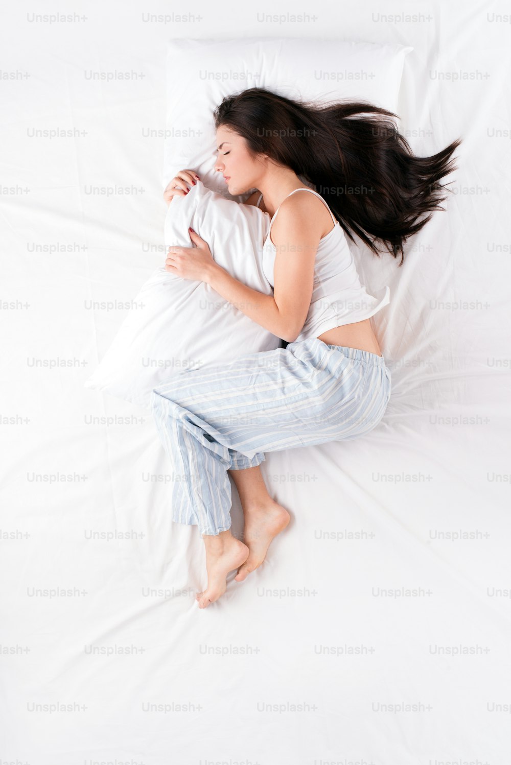 Hermosa mujer joven durmiendo en posición fetal y sosteniendo la almohada