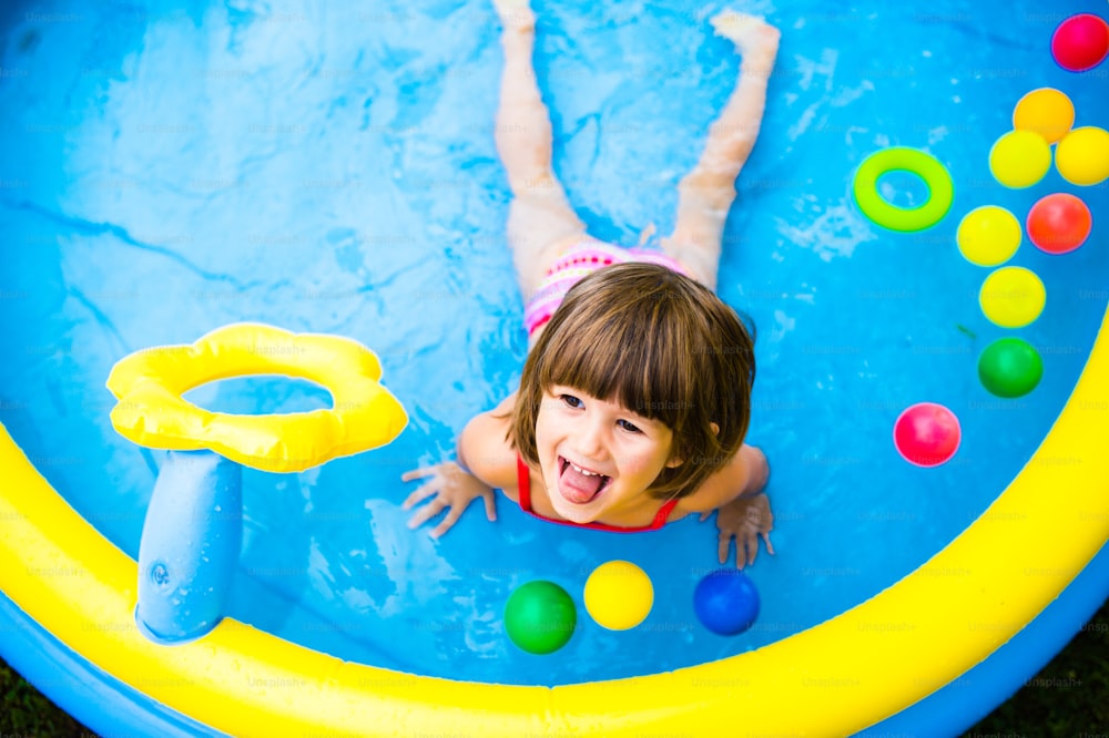 Cute little girl having fun in blue garden swimming pool. Sunny summer day at the backyard