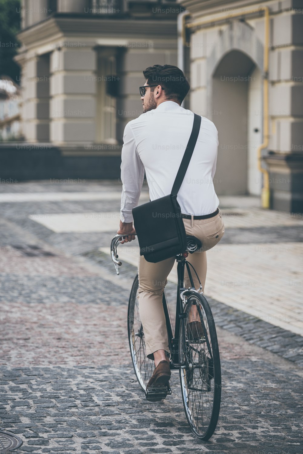 Vista traseira do jovem de óculos olhando para o lado enquanto anda de bicicleta