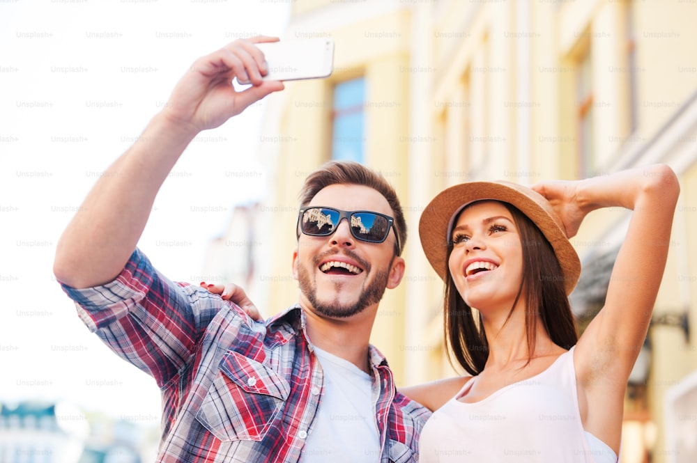 Vue en contre-plongée d'un jeune couple d'amoureux heureux faisant du selfie tout en se tenant à l'extérieur ensemble