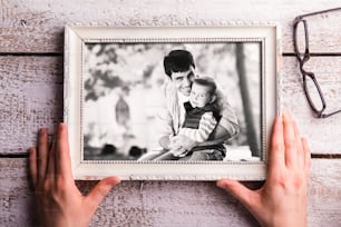 Fathers day composition. Hands of unrecognizable man holding black and white picture of father holding his little son. Studio shot on white wooden background.