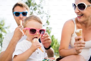 Young parents with their little son in colorful sunglasses eating ice cream, sunny summer garden