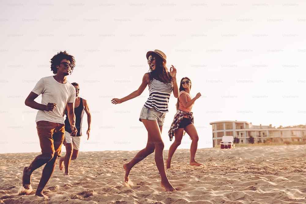 Gruppo di giovani allegri che corrono lungo la spiaggia e sembrano felici