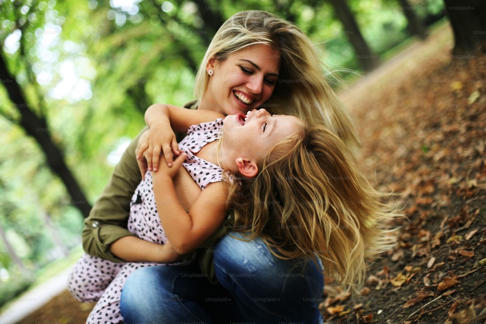 Mutter mit ihrer Tochter spielt im Park. Mutter umarmt ihre Tochter und beide lachen.