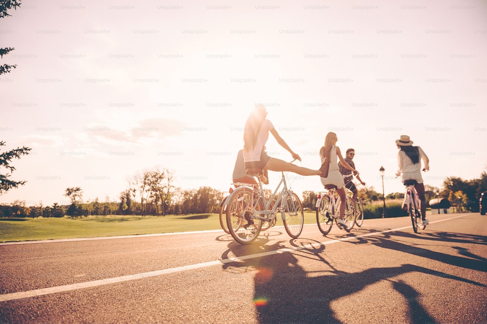 Low angle view of young people riding bicycles along a road and looking happy