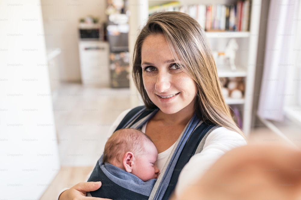 Belle jeune mère avec son fils nouveau-né en écharpe de portage prenant un selfie