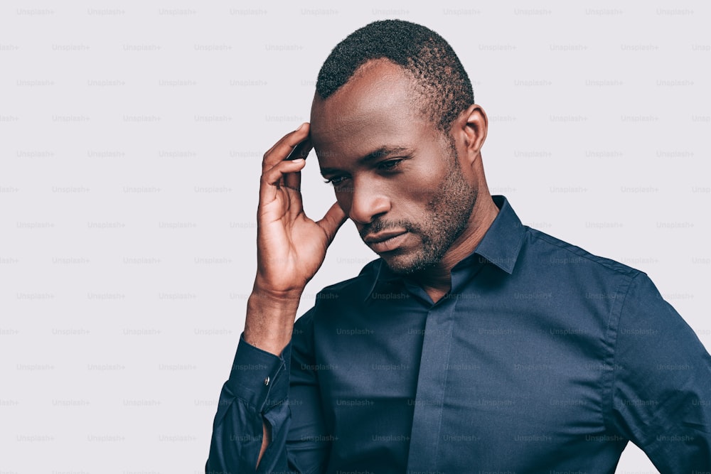Handsome young African man touching head with hand and looking uncertain while standing against grey background