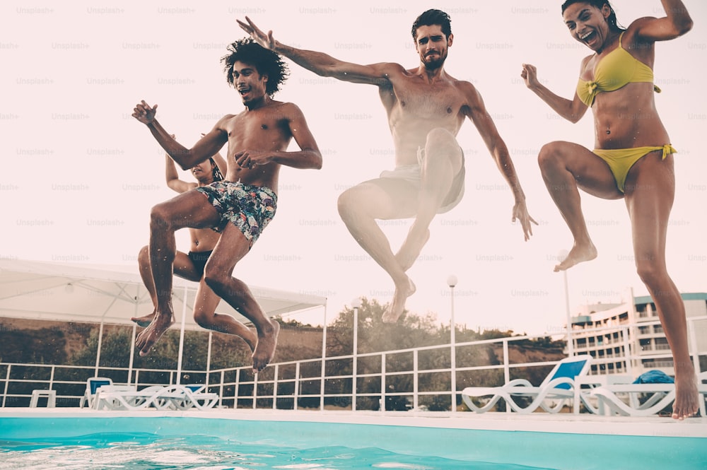 Group of beautiful young people looking happy while jumping into the swimming pool together