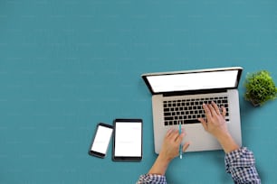 Scrivania da ufficio con schermo vuoto di tablet, smartphone e uomo che utilizza computer portatile. Vista dall'alto.