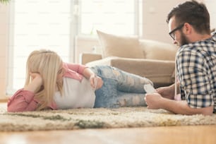 Couple in love lying on the carpet on the floor, playing cards and enjoying their leisure time. Selective focus, lens flare effect on the window.