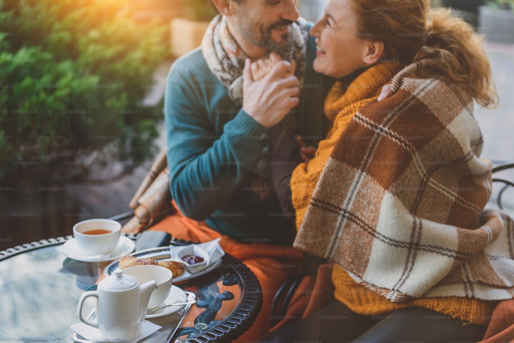 Happy married couple is warming up by their love in autumn. They are sitting at table and hugging. Lovers are smiling