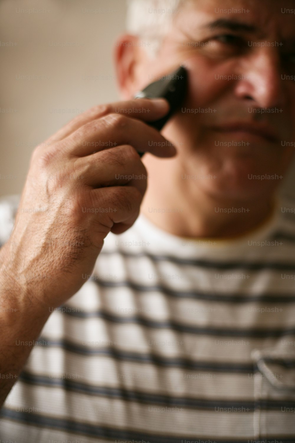 電気カミソリを使って自宅で髭を剃る先輩男性。 手元に焦点を合わせる。