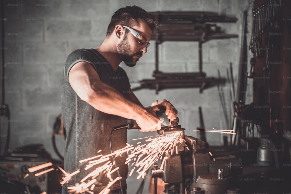 Confident young man grinding with sparks in repair shop