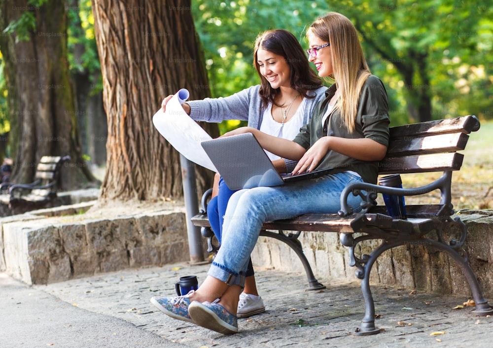 Portrait of two businesswomen sitting in park with laptop and blueprints. Business team working online togetherness while consulting.