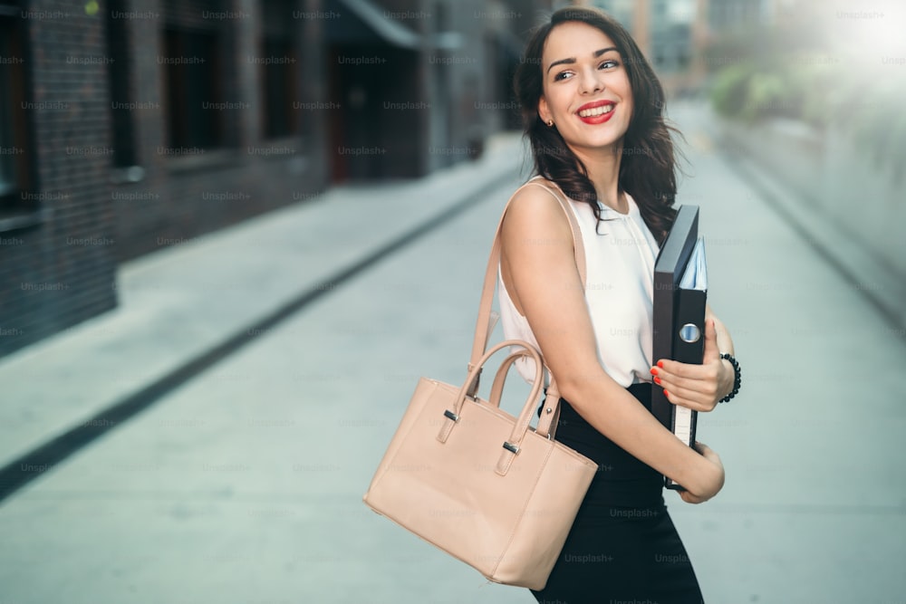 Beautiful businesswoman carrying folders outdoors