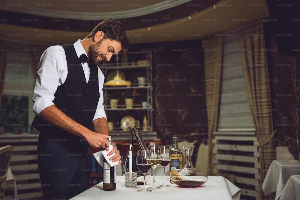 Fascinated man is opening beverage. Many utensils on table