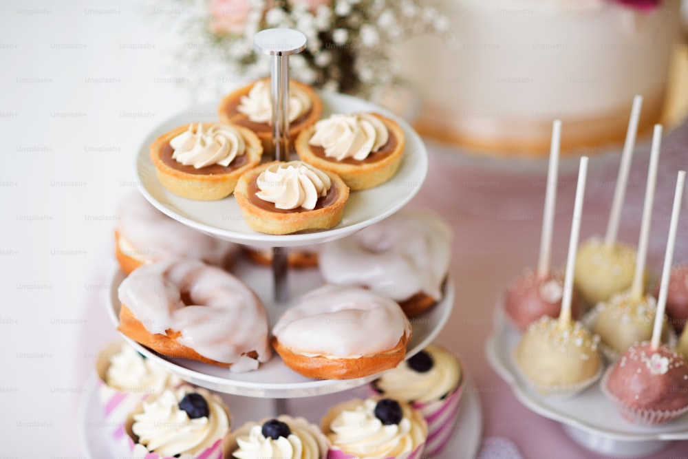 Tarts with meringues, glazed cream puffs or profiterole and cupcakes on cakestand. Cake pops on plate.