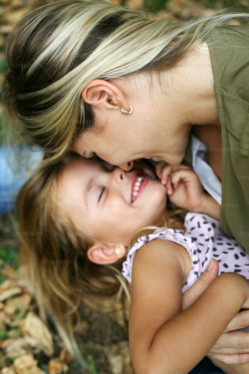 Giovane madre che tocca con il naso la figlia ed entrambe sorridono. Bambina sdraiata sul grembo della madre.