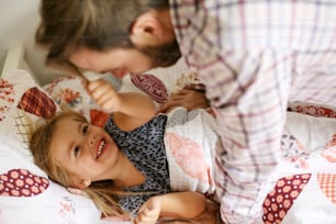 Petite fille s’amusant avec son père avant de dormir. L’accent est mis sur la petite fille.