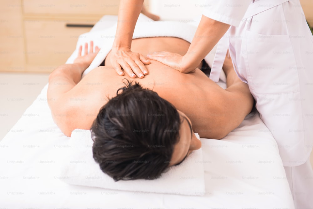 Relaxed man is enjoying back massage at wellness center. He is lying on table with relaxation