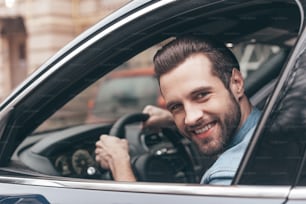 Selbstbewusster junger Mann lächelt und schaut in die Kamera, während er ein Auto fährt