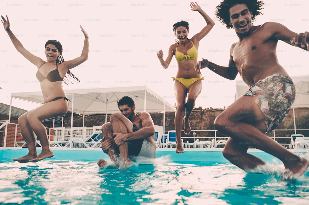 Gruppe schöner junger Leute, die glücklich aussehen, während sie zusammen ins Schwimmbad springen