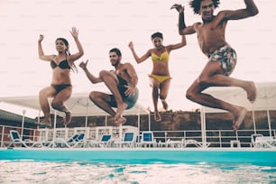 Gruppo di bei giovani che guardano felici mentre saltano insieme in piscina