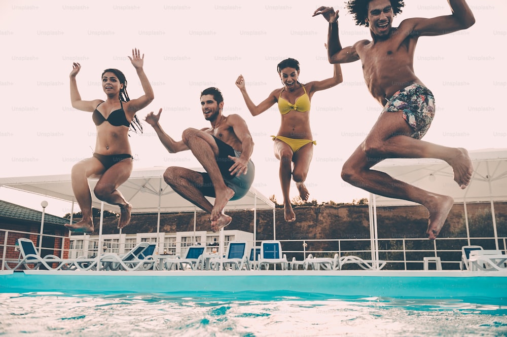 Gruppo di bei giovani che guardano felici mentre saltano insieme in piscina