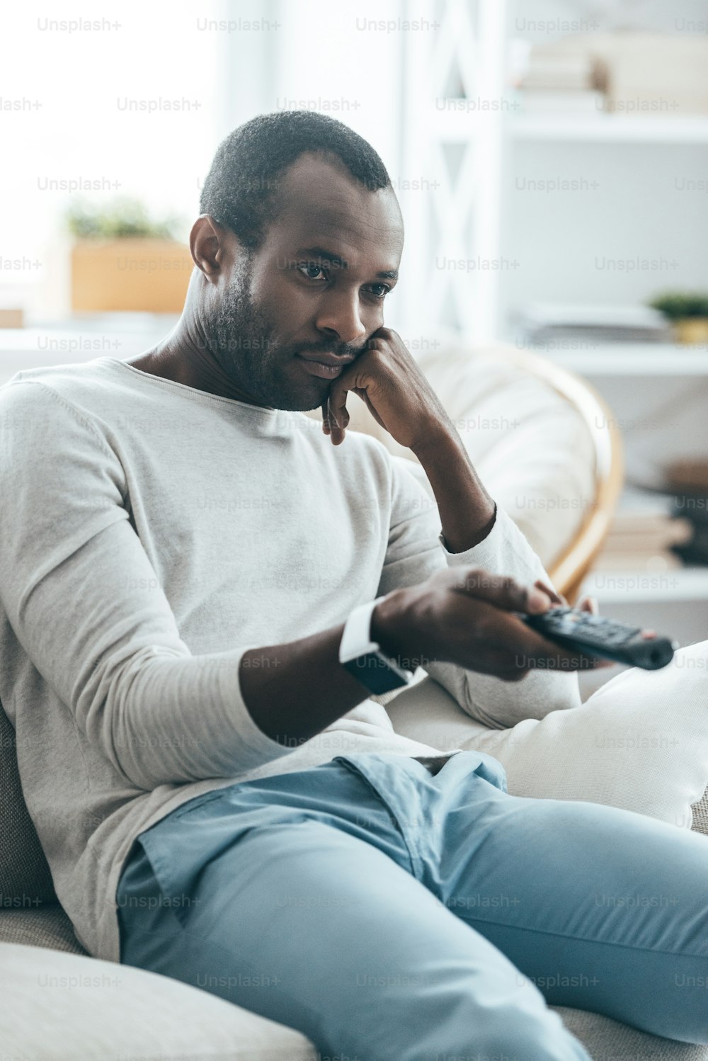 Apuesto joven africano sosteniendo un control remoto mientras está sentado en el sofá de su casa