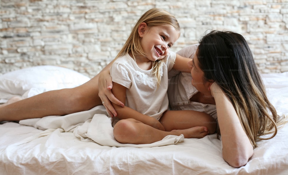 Mother and daughter enjoy in bed at home and looking each other.