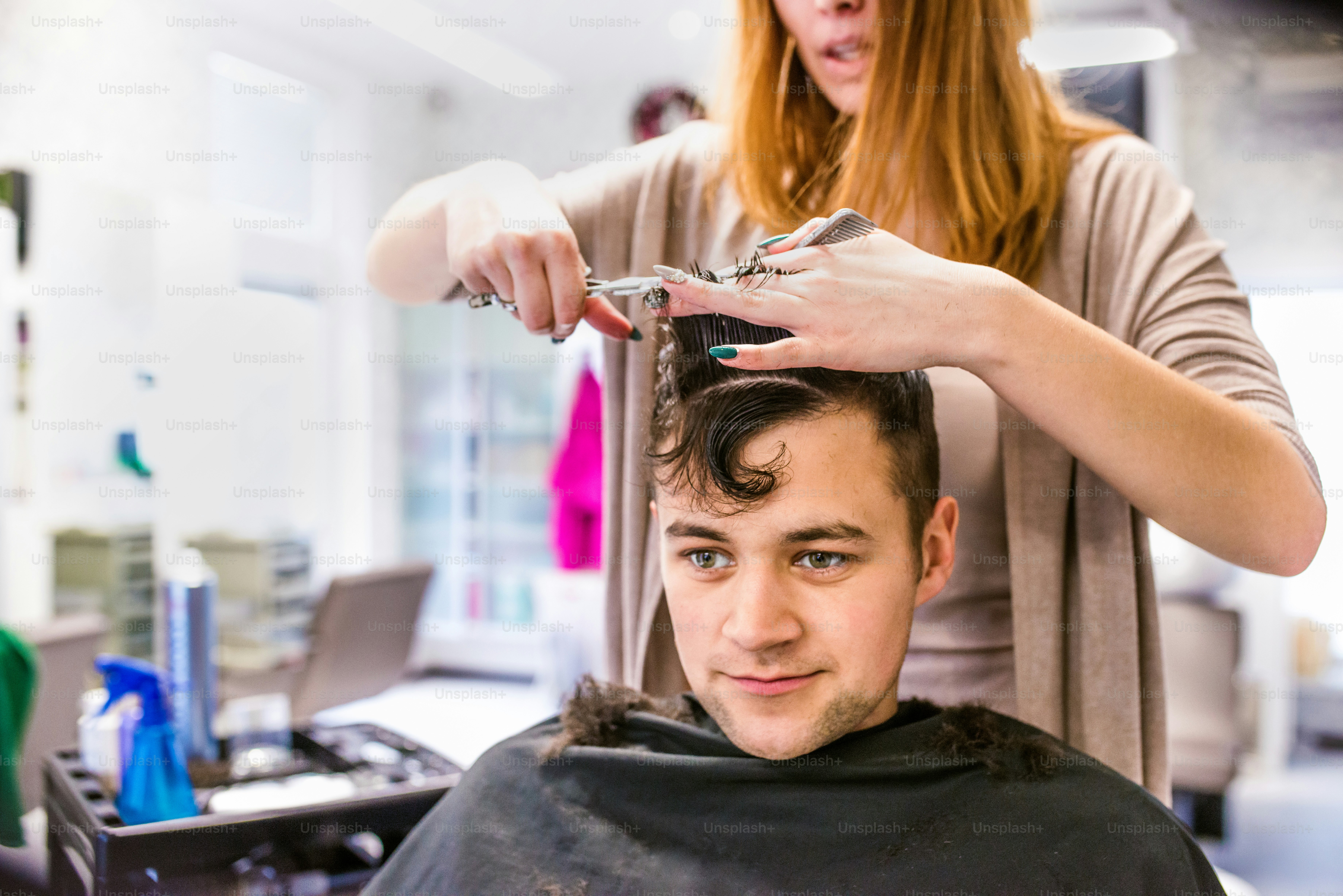 Nicht erkennbare professionelle Friseurin schneidet Haare ihres jungen Kunden und macht einen neuen Haarschnitt. Friseur bei der Arbeit. Mann im Friseursalon.