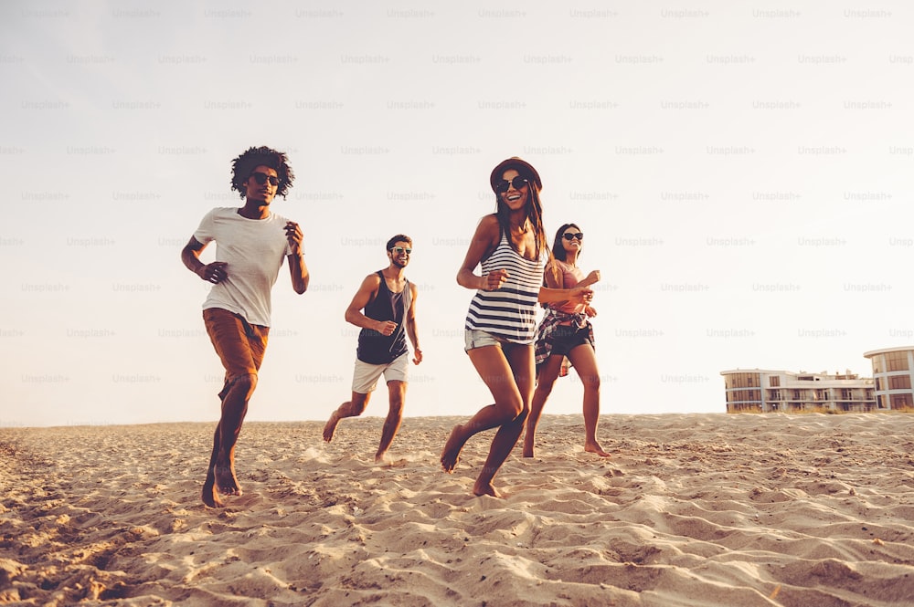 Gruppo di giovani allegri che corrono sulla spiaggia e sembrano felici