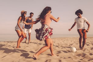 Group of cheerful young people playing with soccer ball on the beach with sea in the background