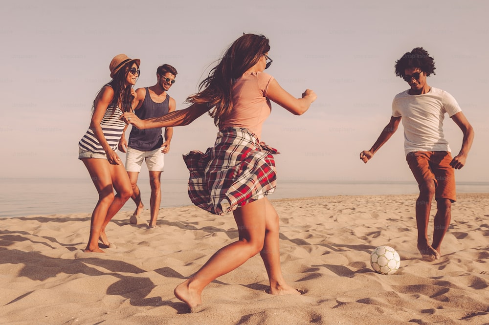 Group of cheerful young people playing with soccer ball on the beach with sea in the background