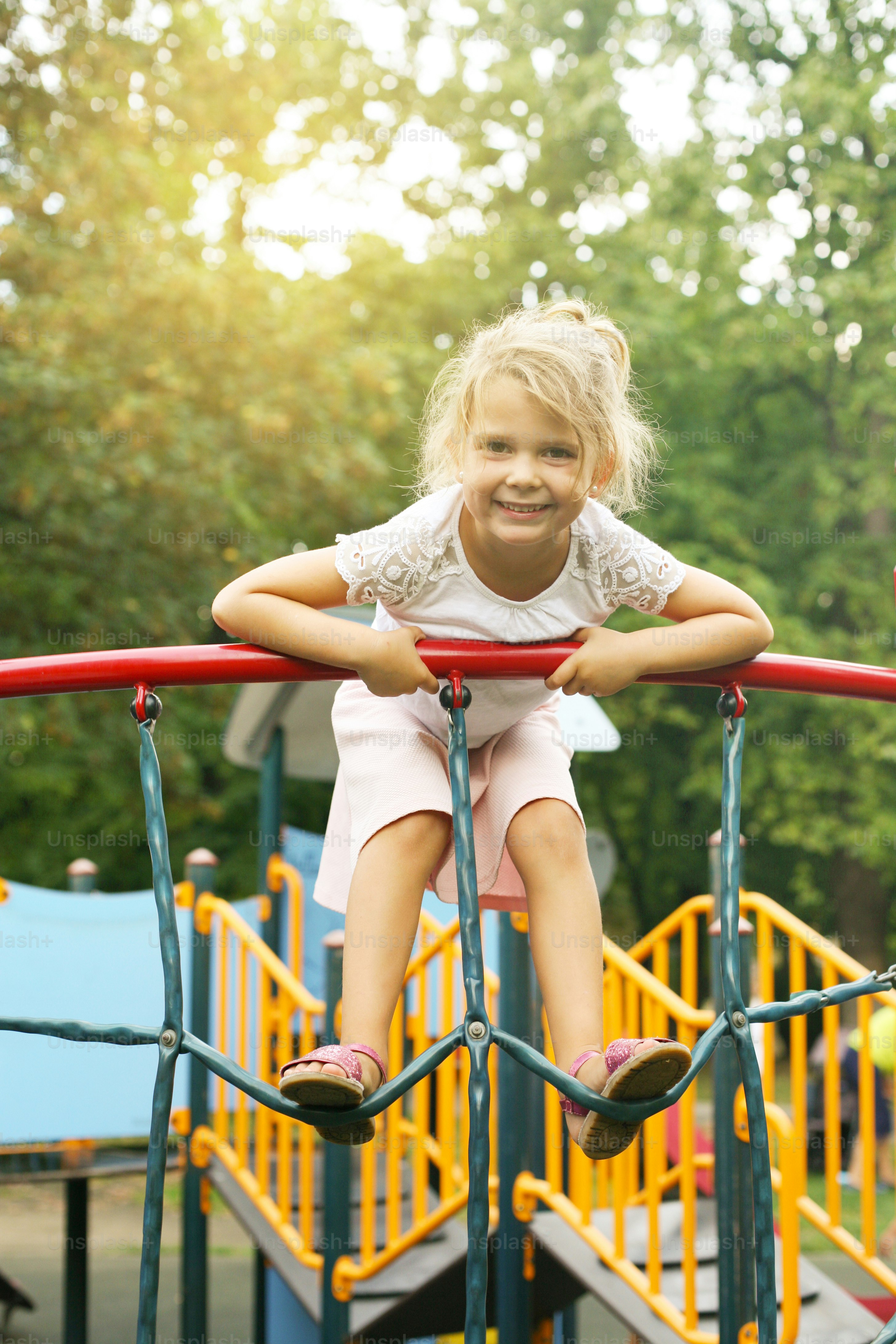 Little girl is climbing at the playground and looking at camera.