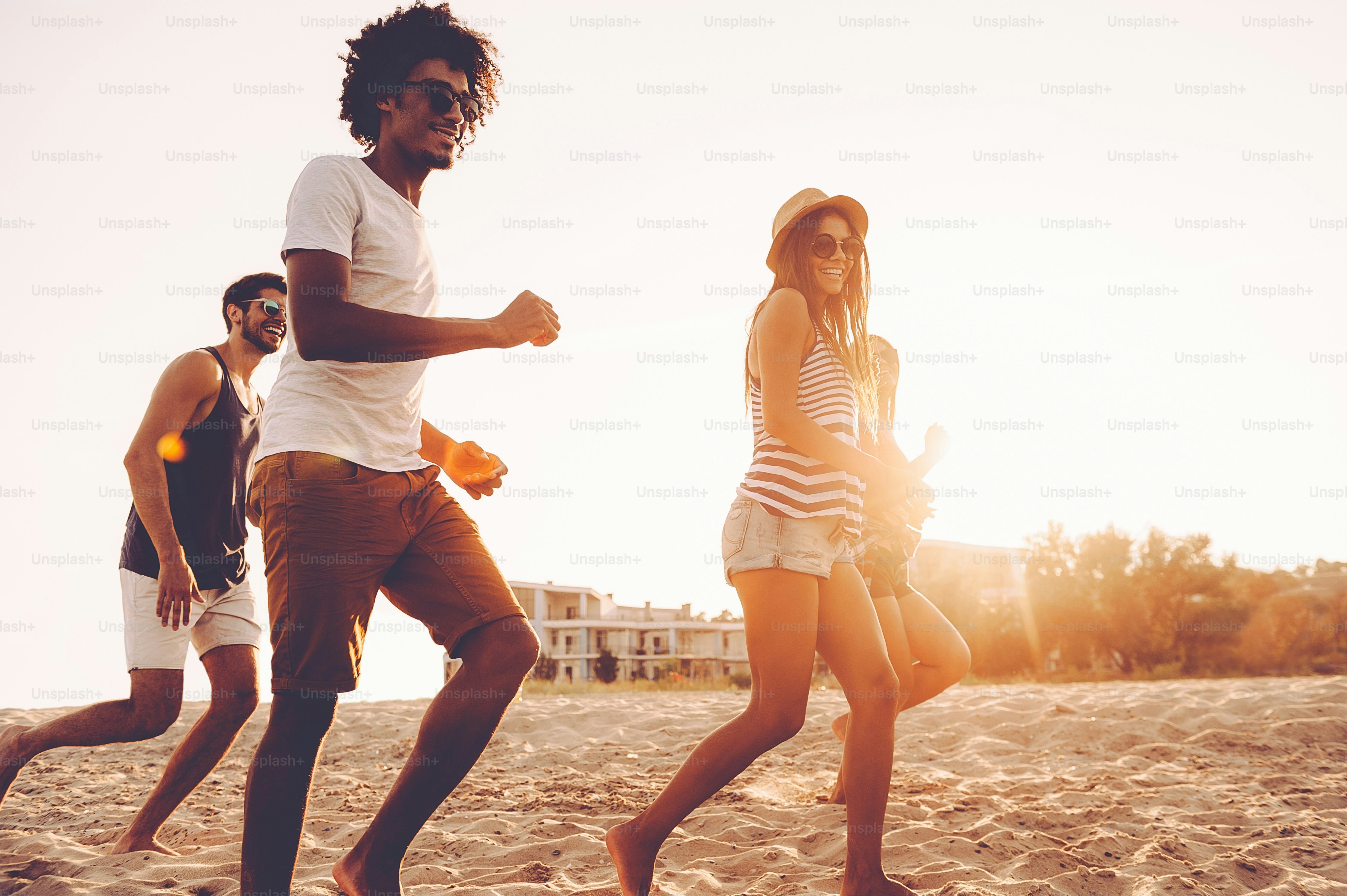 Groupe de jeunes gens joyeux courant le long de la plage et ayant l’air heureux