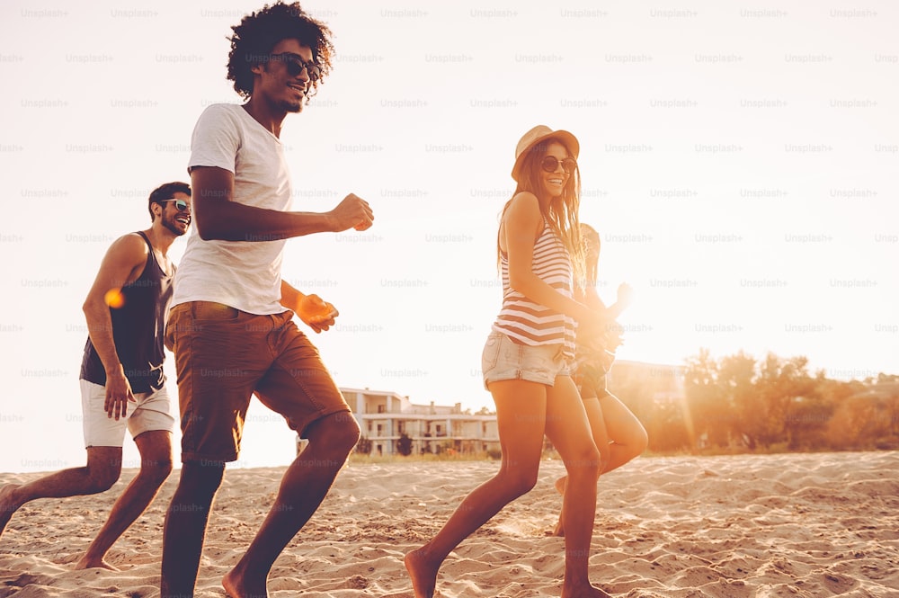 Grupo de jóvenes alegres corriendo por la playa y luciendo felices