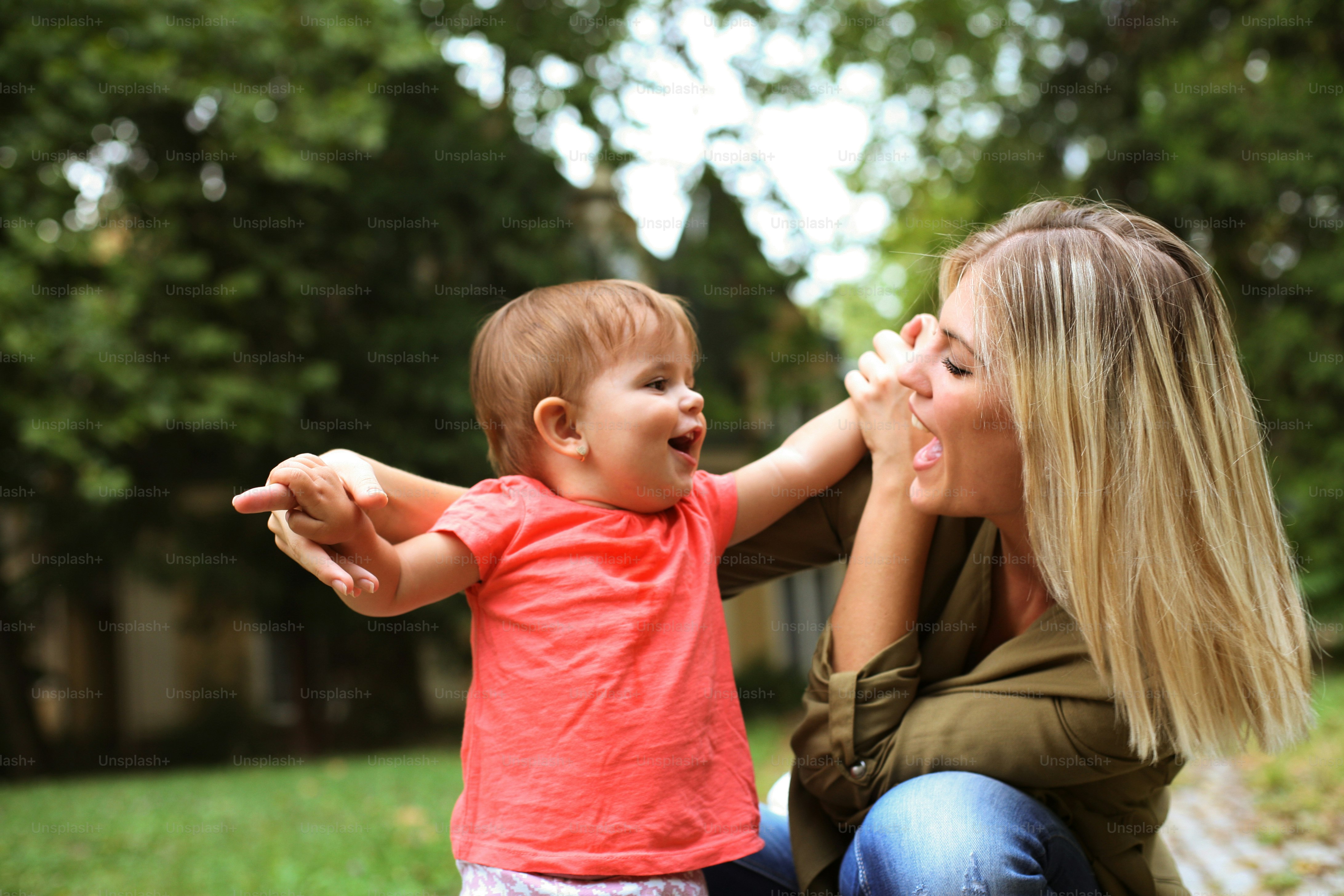 Ibu muda menyentuh dengan hidungnya bayi perempuan yang bahagia dan keduanya tersenyum.