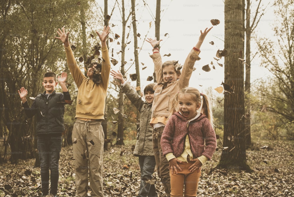 Grupo de niños y niñas jugando en hojas de otoño en el parque.