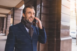 Happy businessman is talking on phone outdoors. He is standing and smiling