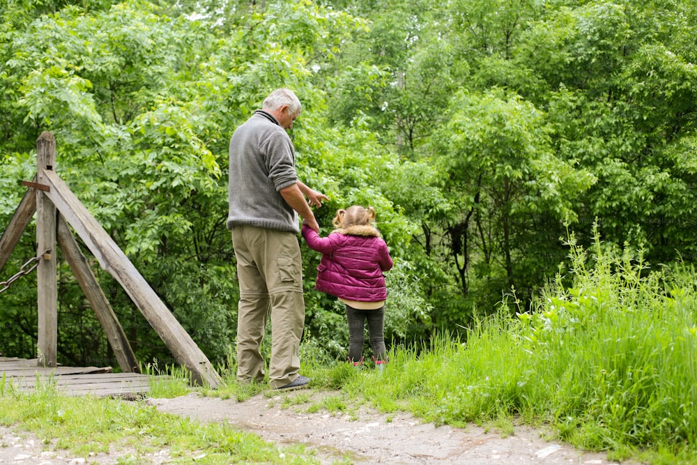 A grandfather with his granddaughter showing her something  in woods.