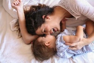 Young mother playing with her baby girl playing in bed.