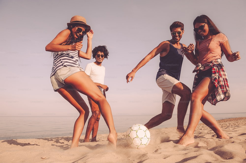 Grupo de jóvenes alegres jugando con la pelota de fútbol en la playa