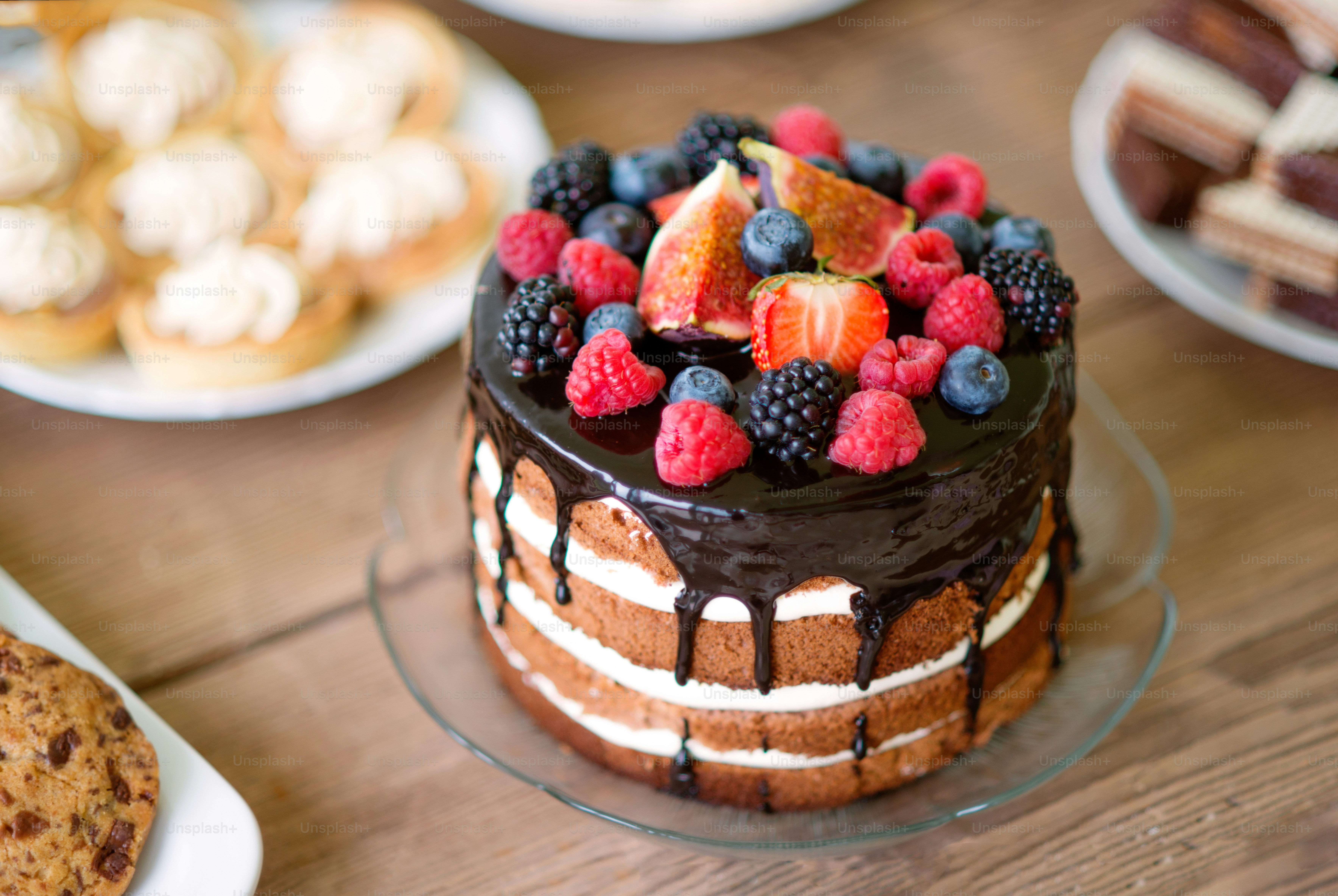 Brown wooden table with naked cake with chocolate and berries, various cookies and tarts. Candy bar. Studio shot.