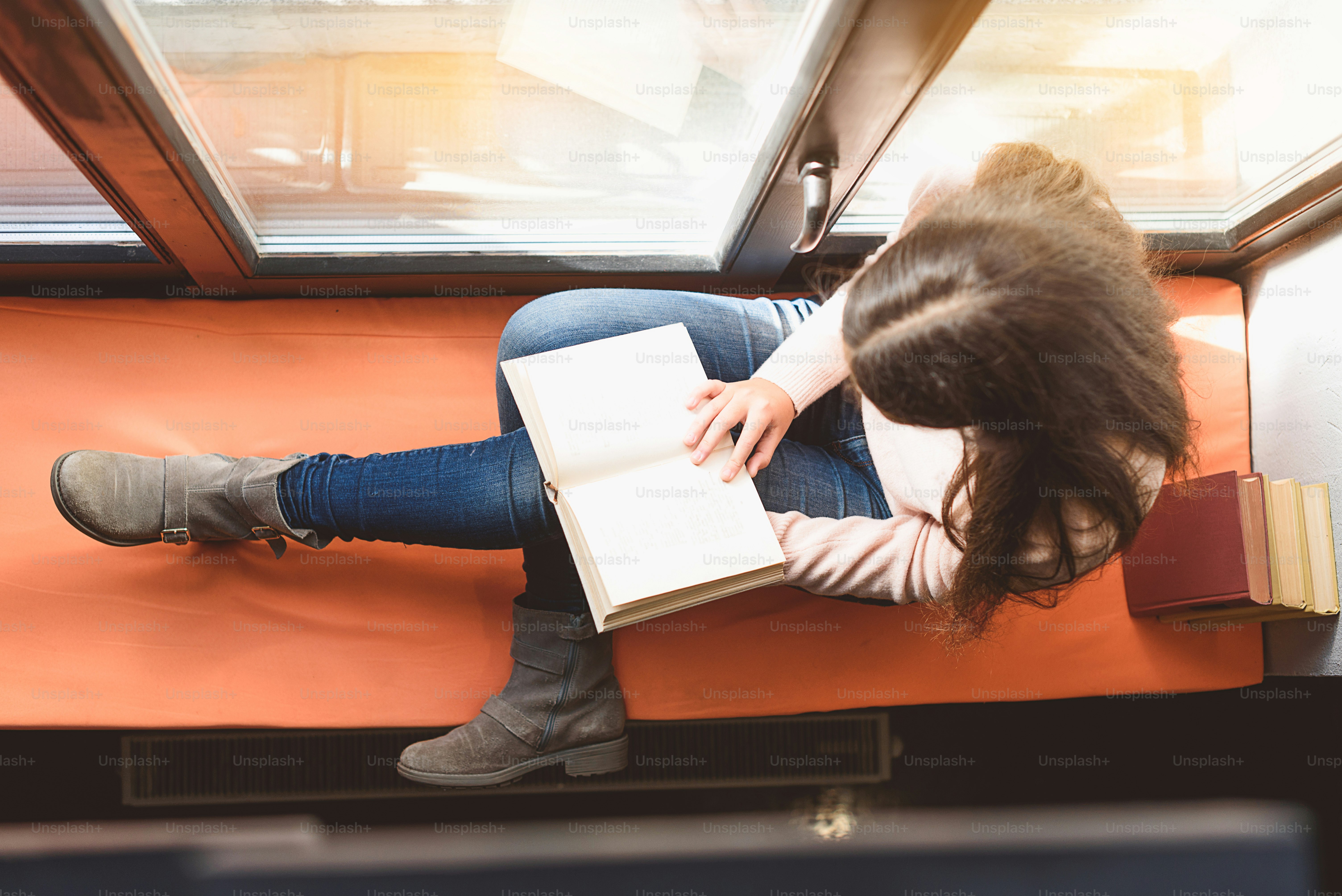 Top view of girl sitting on windowsill, she is holding volume at her knees
