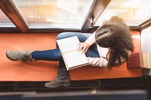 Top view of girl sitting on windowsill, she is holding volume at her knees