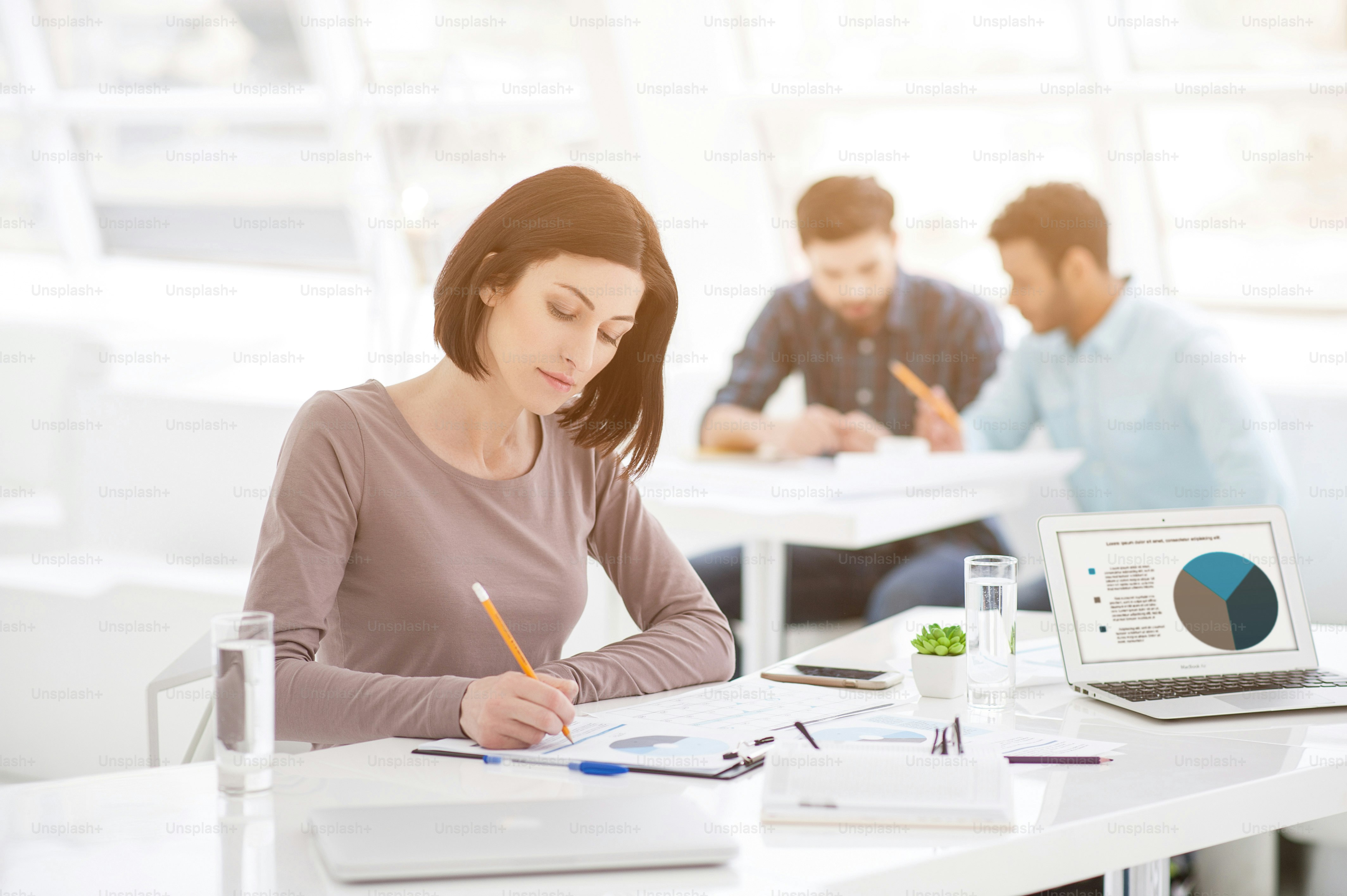Old project, new ideas. Business woman making notes with her staff in background at modern bright office indoors