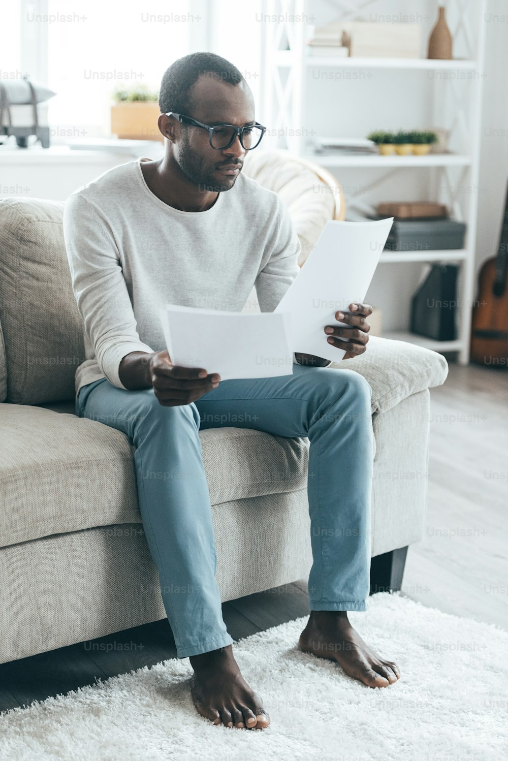 Beau jeune homme africain lisant des documents assis sur le canapé à la maison