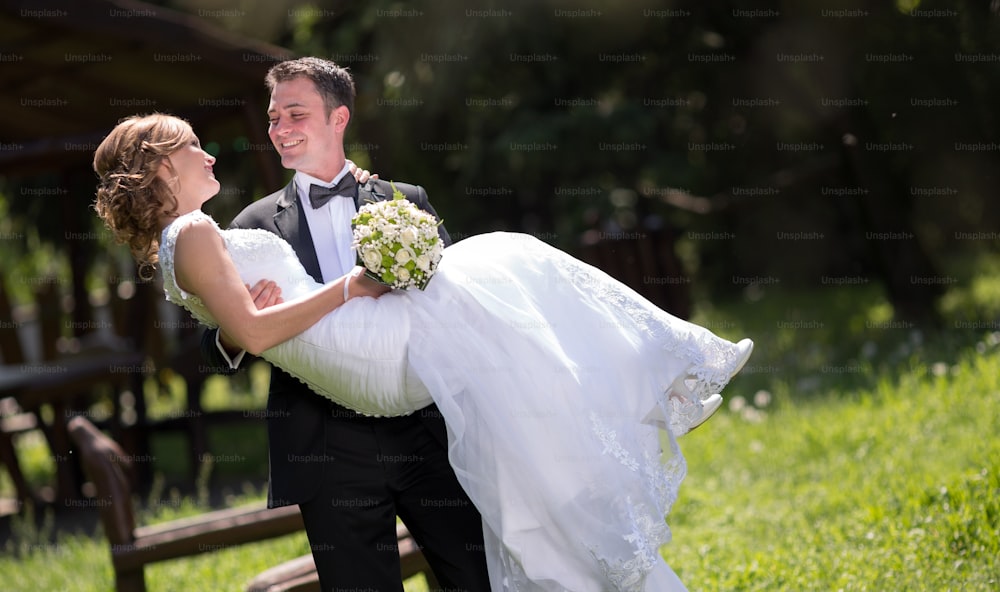 Bräutigam trägt Braut draußen und lächelt
