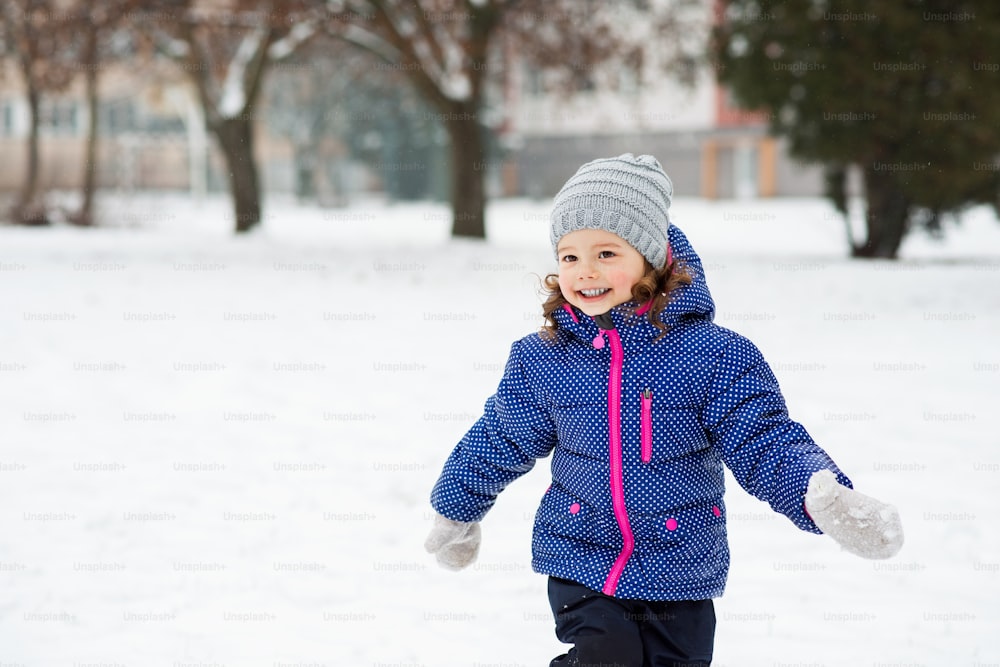 Cute little girl in blue jacket and knitted hat playing outside in winter nature, running around